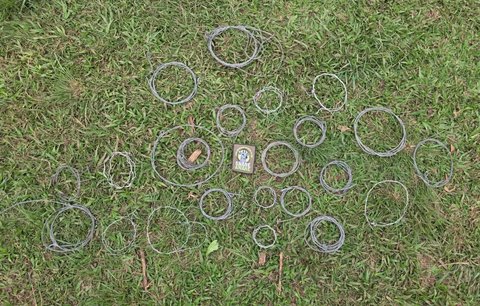 23 coiled wire snares laid out on grass around the Snare Aware emblem